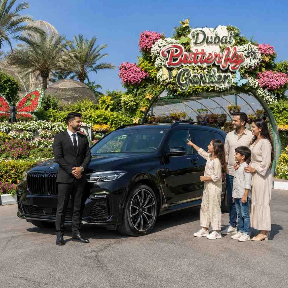 Family arriving at Dubai Butterfly Garden in a luxury BMW X7 with a professional chauffeur standing beside the SUV outside the colorful garden entrance.